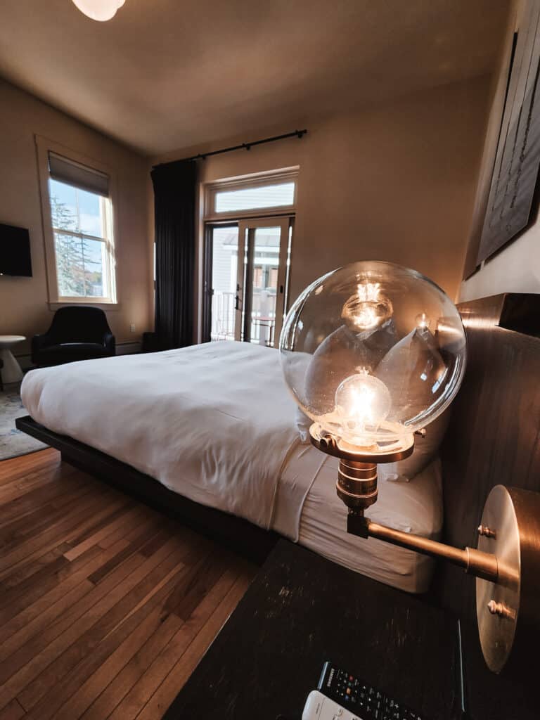 a vintage style globe light bulb next to a made bed in a hotel room, the light is lit
