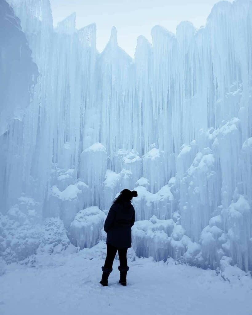 amy, standing in silhouette in winter clothes in front of an impressive wall of ice, the ice castles of new hampshire
