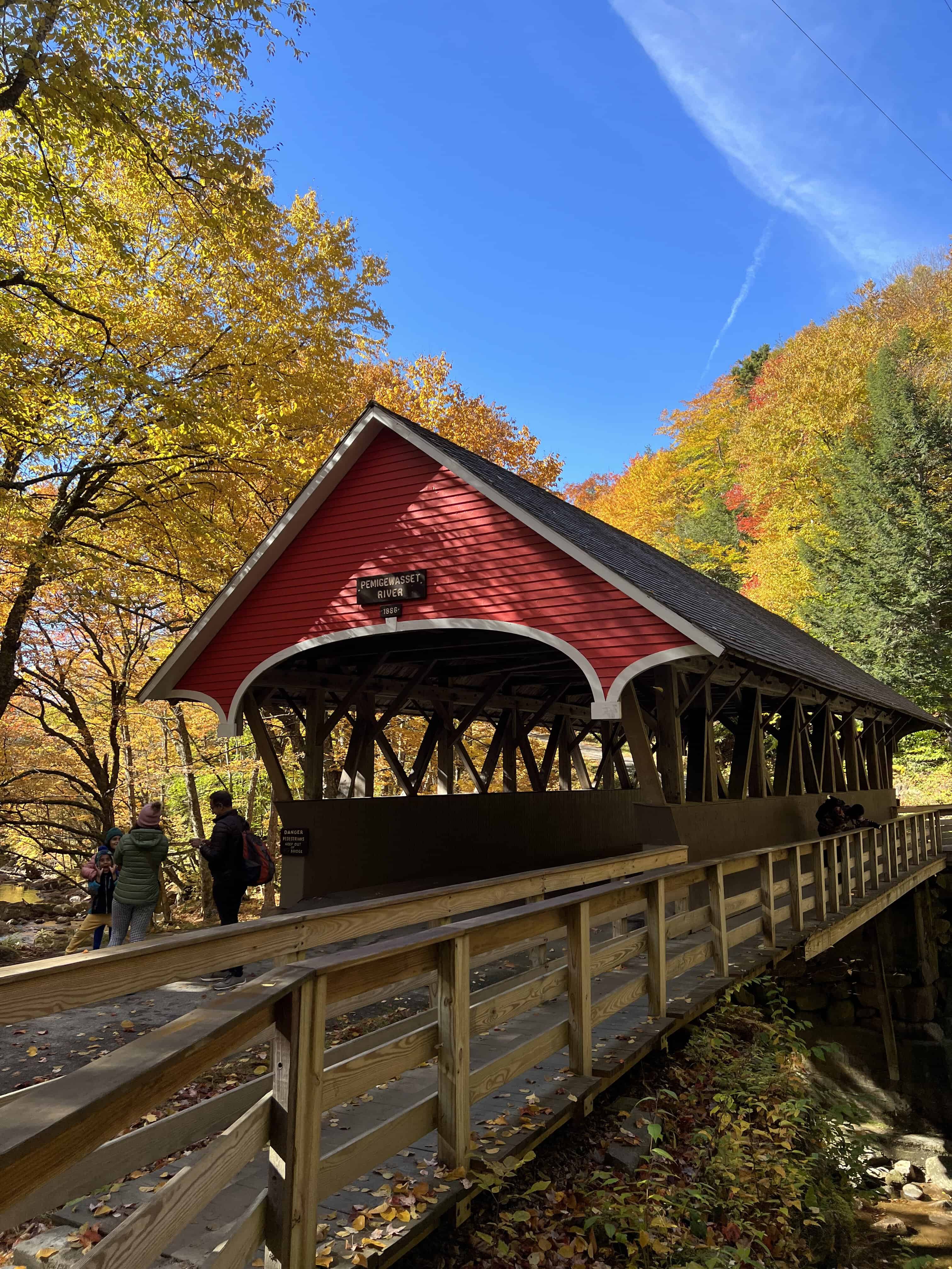 image of a narrow red covered bridge with bright fall foliage behind