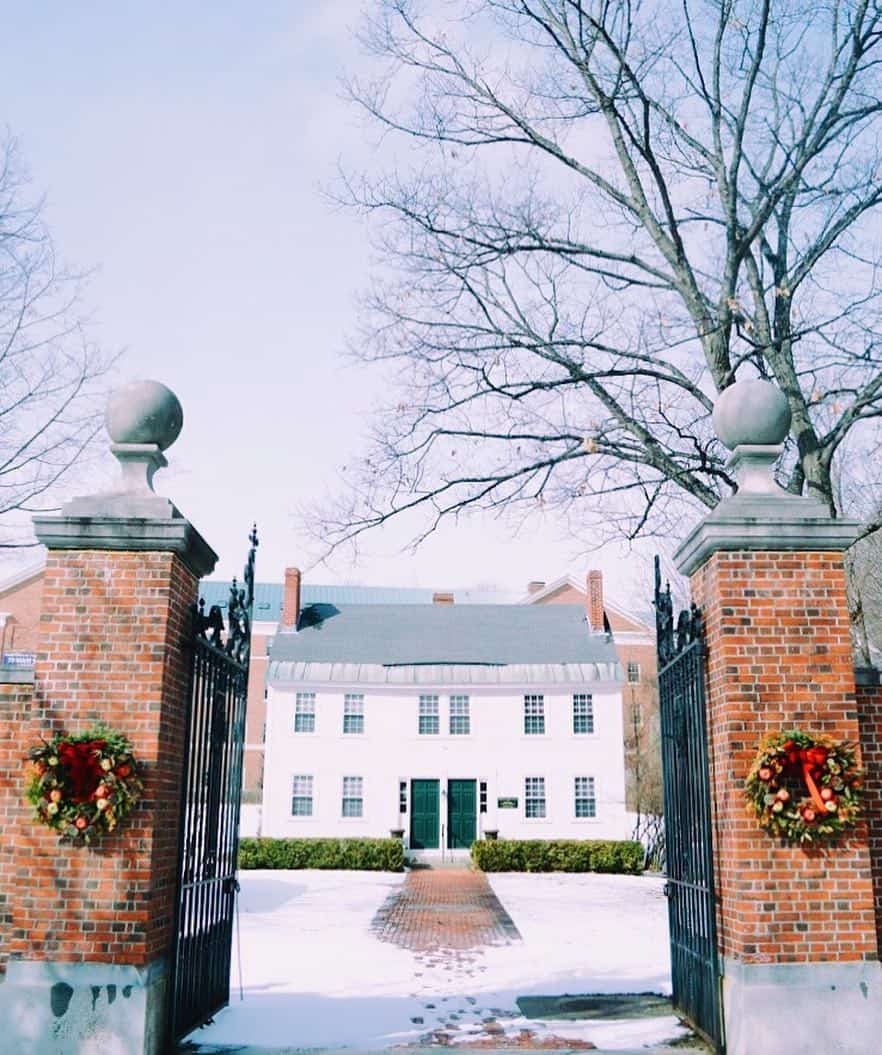a festive colonial home in the snow with two brick columns bearing christmas wreaths