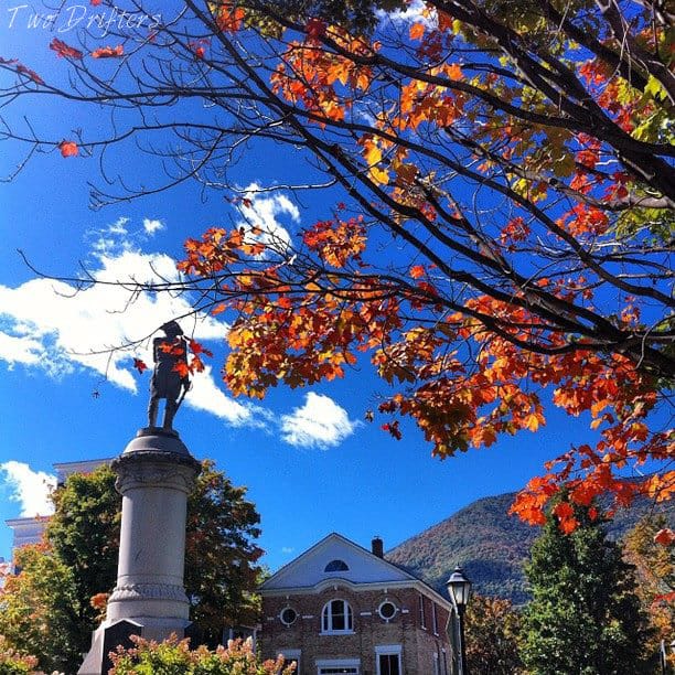 a fall tree and statue with a distant mountain and building: manchester VT