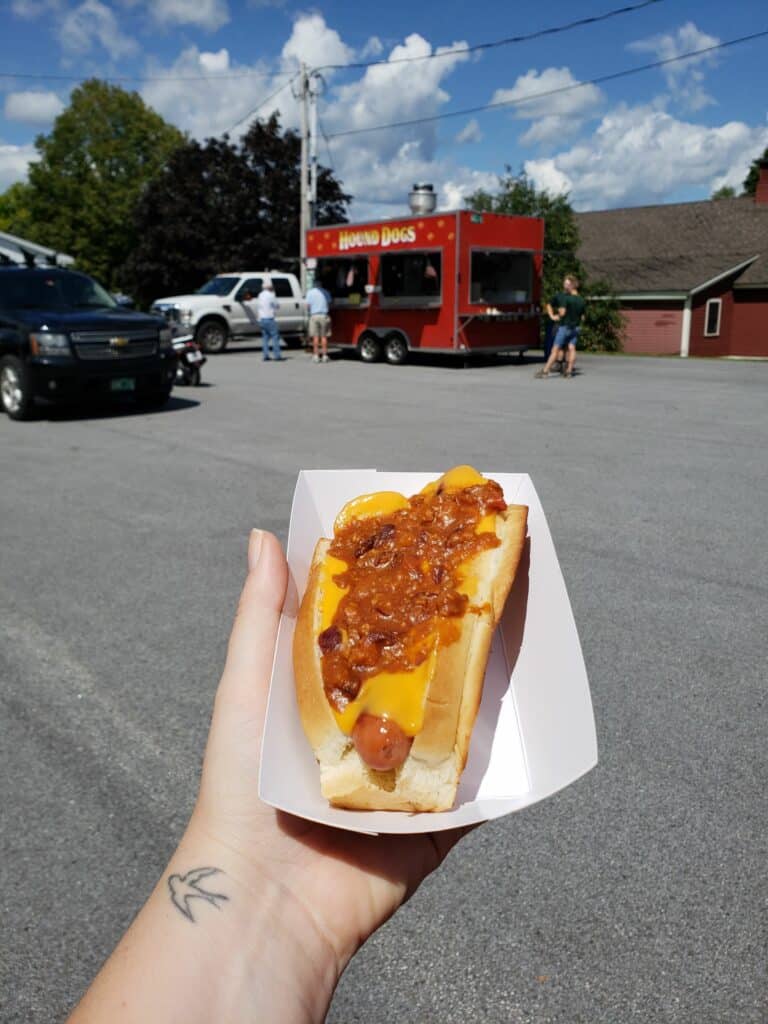 a hand holds a chili dog in a parking lot