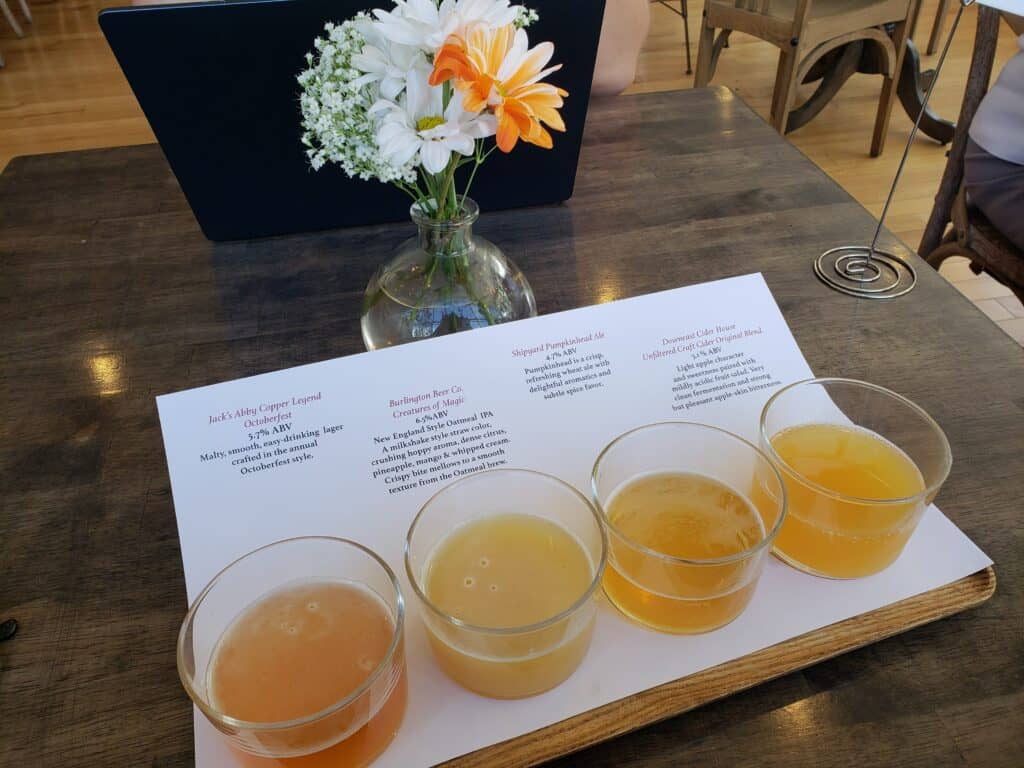a flight of 4 light beers sits on a table in front of a small vase of flowers