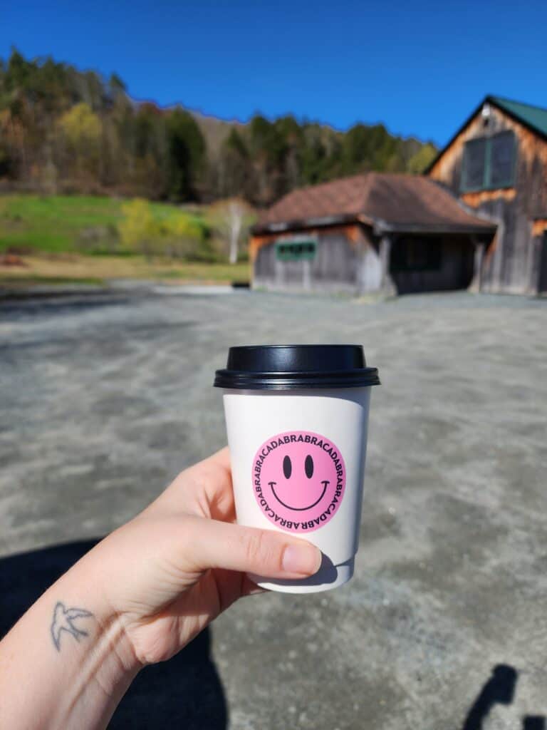hand holding a coffee cup with a smiley face in front of a blurry barn