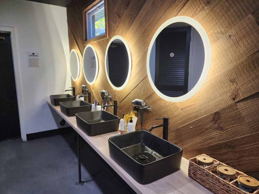 a modern public bathroom interior with illuminated round mirrors, black bucket sinks, and a wooden backdrop. this evokes a calm, cozy vibe