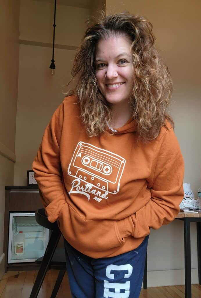 amy posing in an orange sweatshirt that says Portland, ME