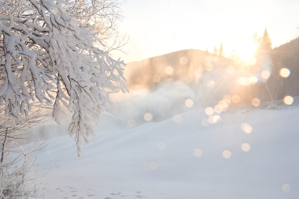 snow sparkles as the sun peeks out from behind a mountain in a winter landscape