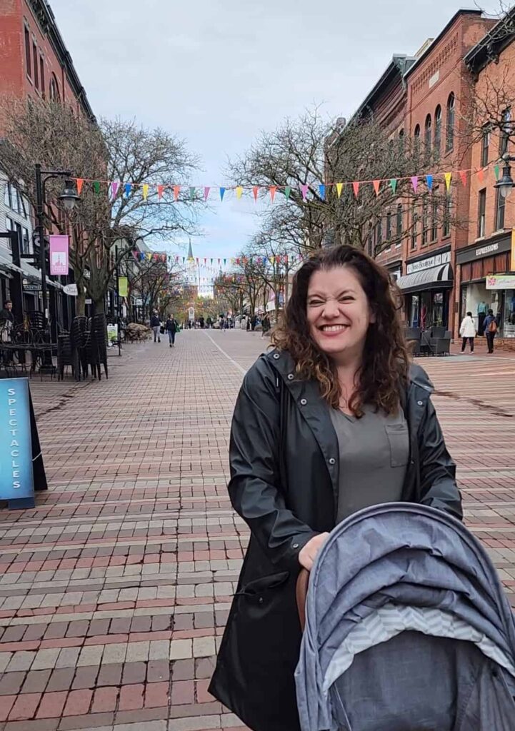 author amy standing in a brick paved plaza with shops on either side and a church steeple in the distance. this is church street in burlington vermont