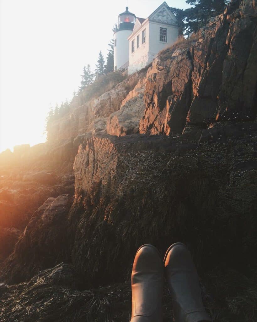 rocky maine coast with a white lighthouse towering overhead, dusk, a pair of boots seen at the bottom as if the photographer is sitting