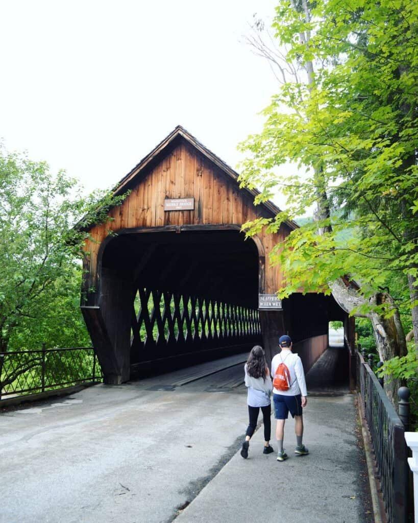 a couple walks towards a classic vermont covered bridge on a summer day