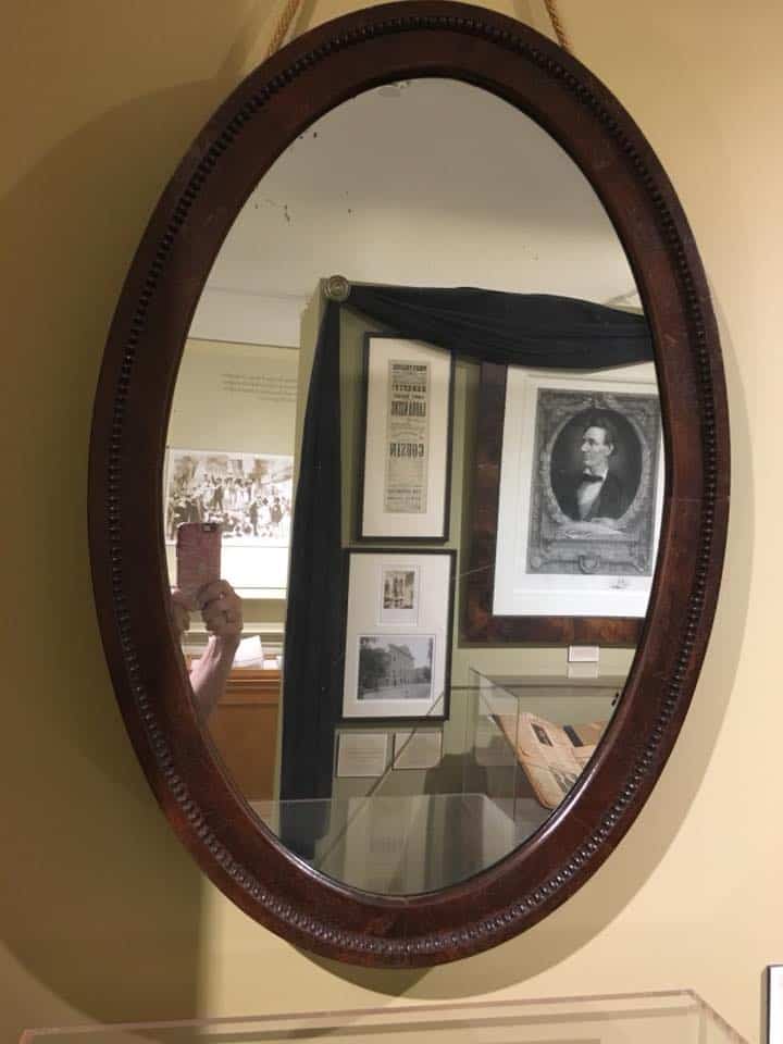 an oval shaped mirror with brown trim, a picture of Abraham Lincoln seen reflected