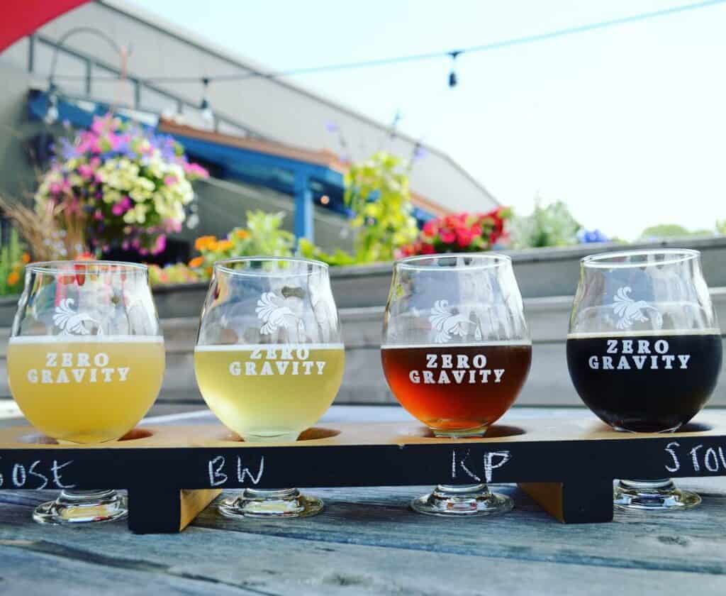 a beer flight on a table with flowers behind, the glasses say zero gravity