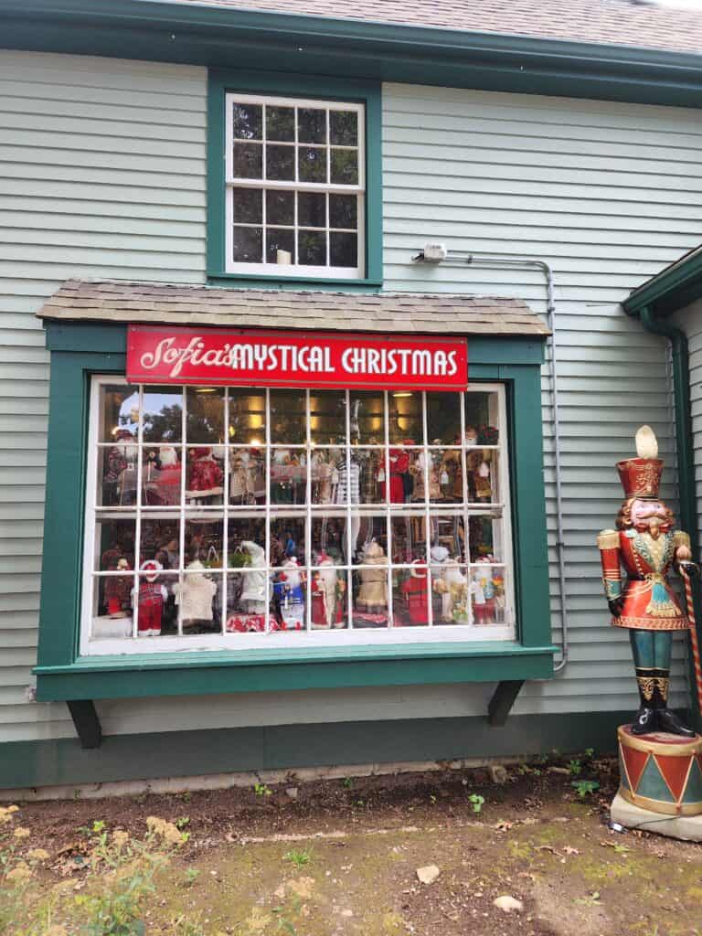 a shop window filled with figures of santa and other holiday items with a sign that says Sofia's Mystical Christmas. there is also a holiday nutcracker outside