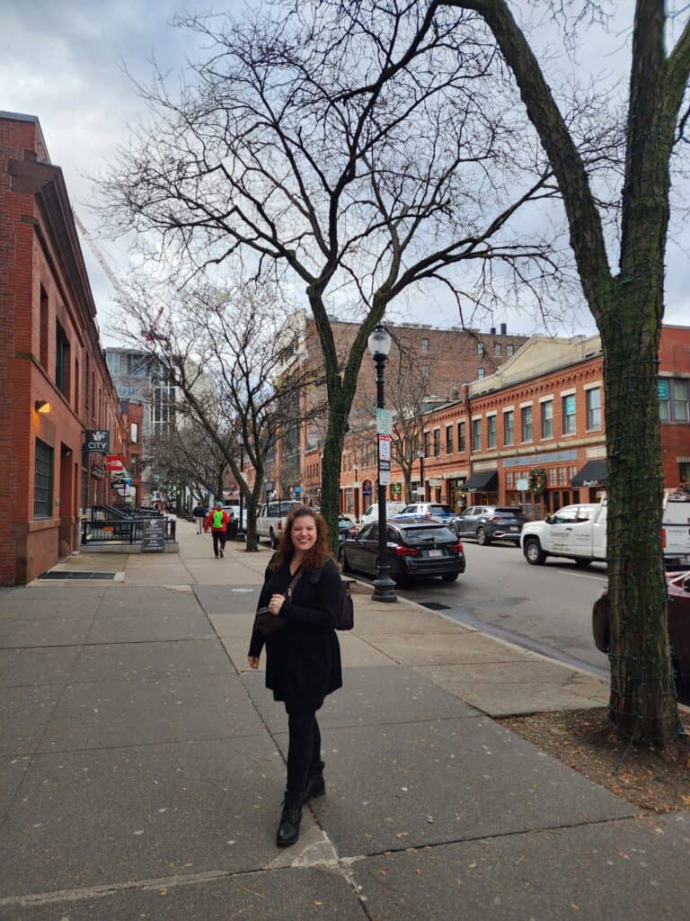 A joyful woman standing on a sidewalk in Boston's historic Back Bay neighborhood, with its charming brownstone buildings and bare trees, a delightful stroll included in the best things to do in Boston