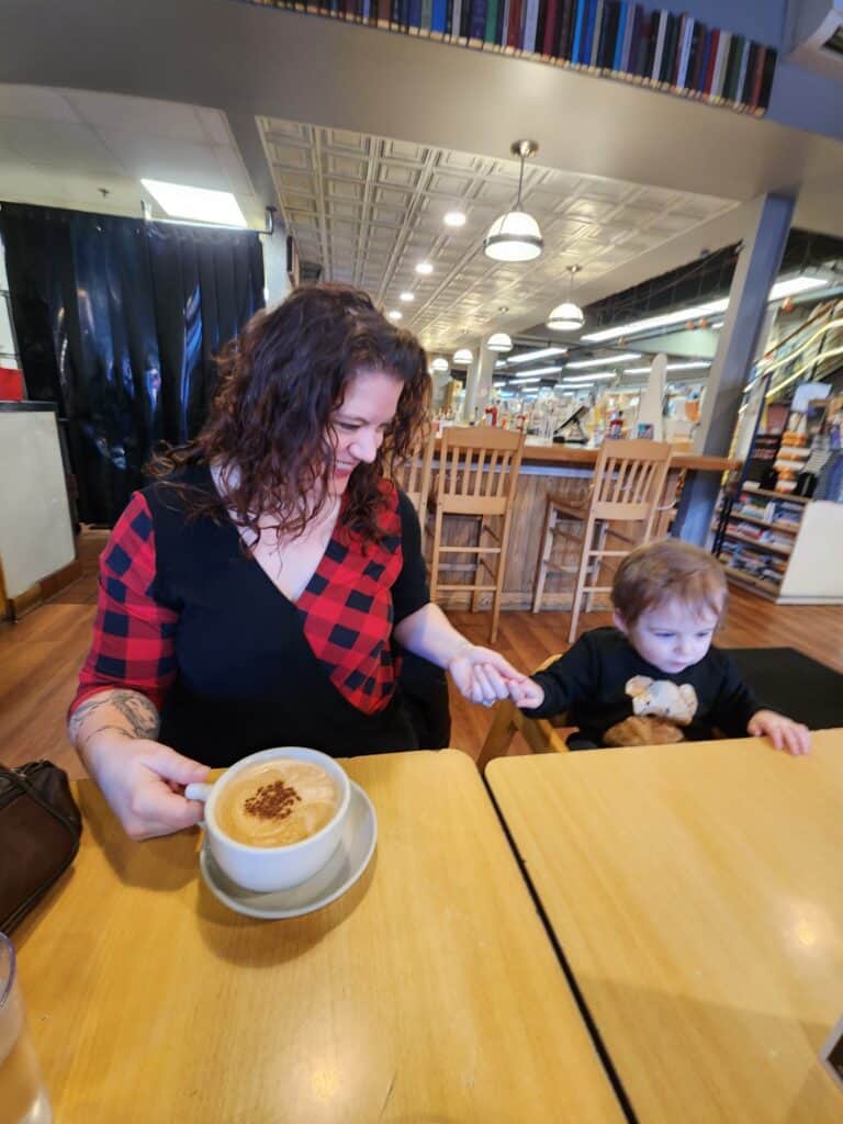 A mother sharing a tender moment with her toddler at a breakfast table in a Boston bookstore cafe, with a latte in foreground