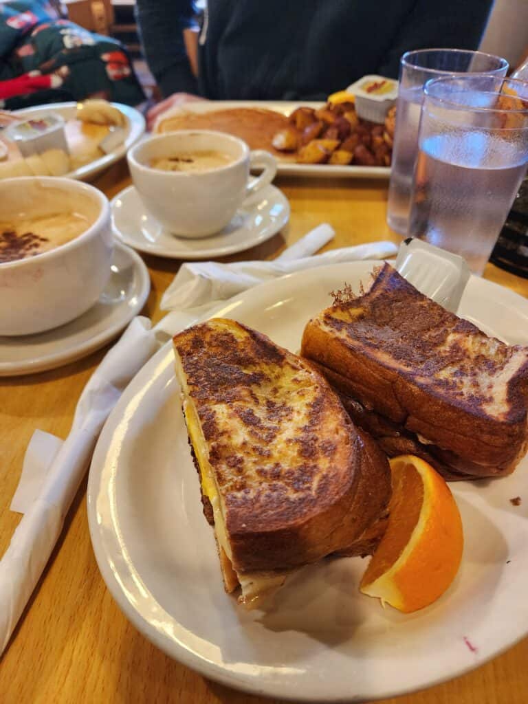 A plate of French toast filled with melting cheese, accompanied by a side of cappuccinos and home fries, served at a popular Boston breakfast spot.