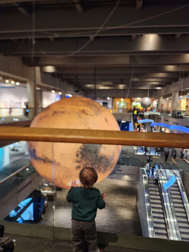 A child gazes in wonder at a large hanging model of Mars in the Museum of Science, Boston, an educational and interactive experience to add to the 'things to do in Boston' list.