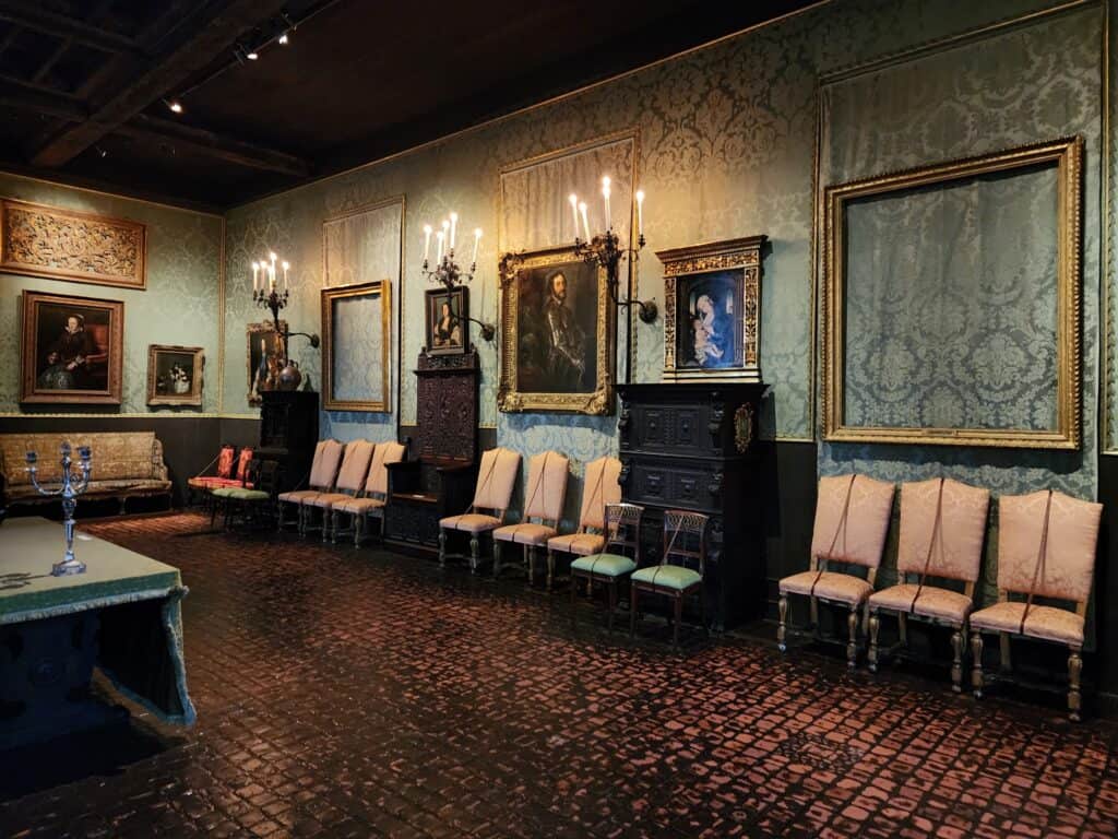 Interior view of a historical room in the Isabella Stewart Gardner Museum, Boston, featuring ornate European Renaissance art, elaborate furniture, and intricate wall tapestries under soft lighting. one frame is empty