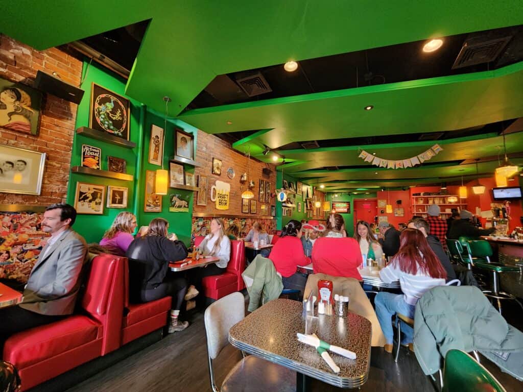 Patrons enjoying breakfast at a vibrant diner in Boston, with red booths, green walls adorned with eclectic art, and a lively atmosphere.