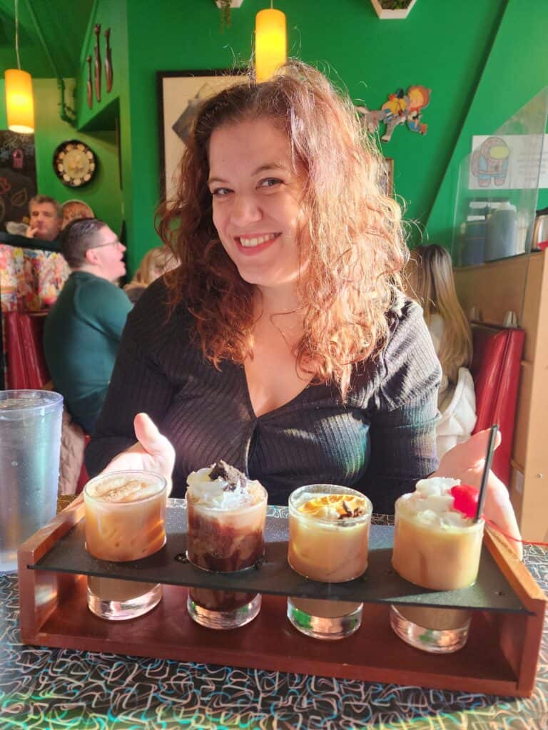 A smiling woman enjoying a selection of gourmet breakfast shooters at a cozy Boston cafe, featuring a warm, sunlit ambiance.