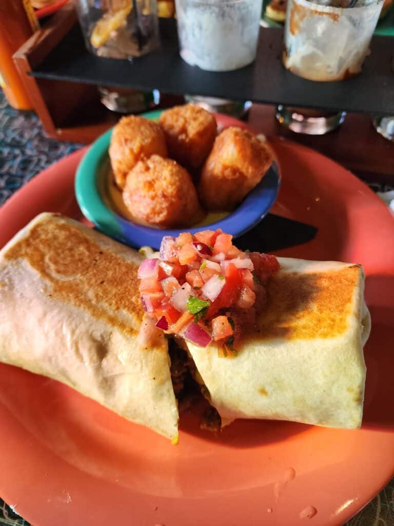 Close-up of a hearty breakfast burrito topped with fresh pico de gallo, served with golden-brown tater tots on a vibrant plate, in a Boston brunch spot.