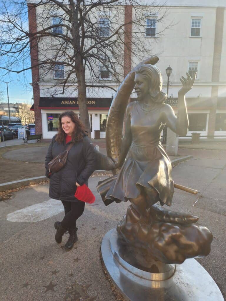 A woman poses next to the Bewitched statue in Salem
