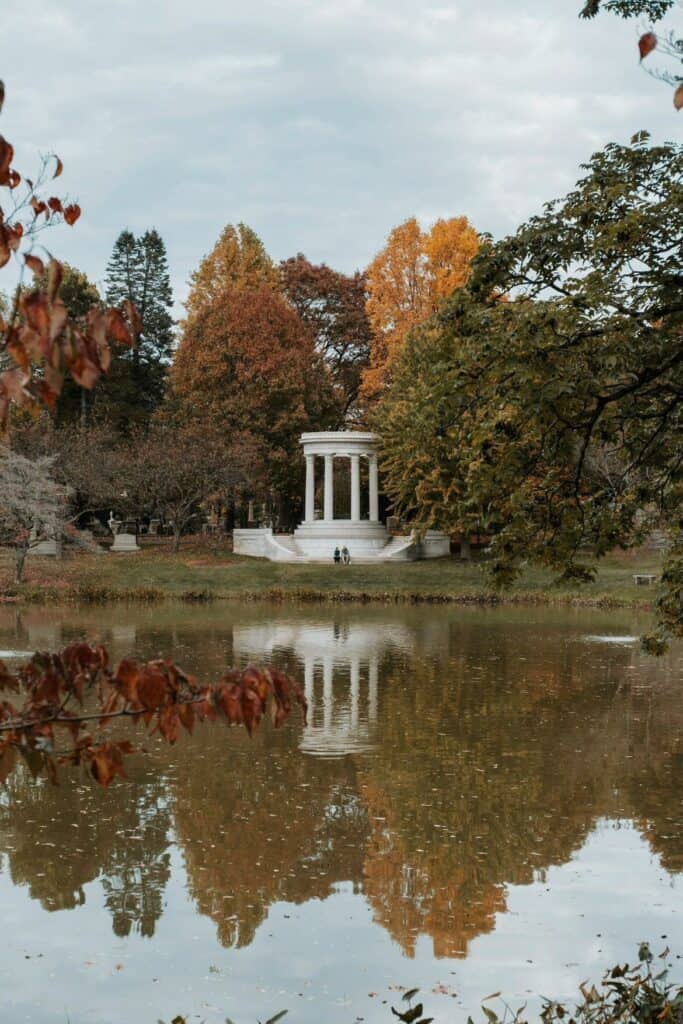Autumn at the Mary Baker Eddy Monument in Mount Auburn Cemetery in Boston, with its classic white gazebo reflected in the tranquil pond amidst a tapestry of fall foliage, a peaceful scene for reflection and nature enjoyment