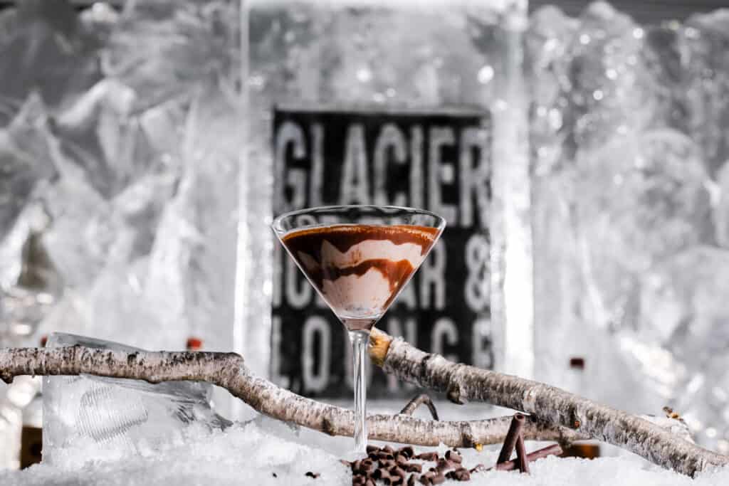 A luxurious chocolate martini served in an elegant glass, set against a backdrop of glistening ice and snow with 'GLACIER' etched signage, evoking the essence of New England winter getaways