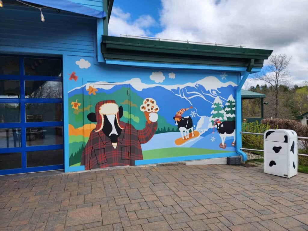 Colorful mural at a Vermont attraction showcasing a whimsical scene with a cow in a flannel shirt, ski slopes, and cows engaging in winter sports, reflecting the state's unique charm and sense of humor.