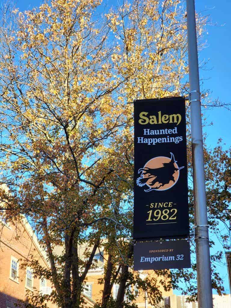 Salem Haunted Happenings sign on pole with autumn foliage beyond