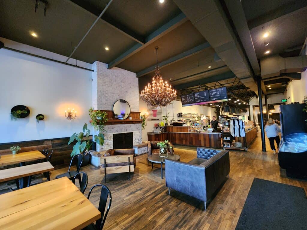 Spacious café in Burlington, Vermont, with an eclectic mix of wooden tables, plush seating, and modern wall planters, highlighted by a striking chandelier and a warm, inviting fireplace