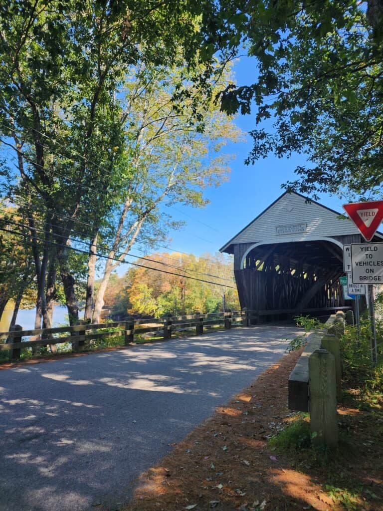 A scenic road in New Hampshire with a covered bridge and fall foliage