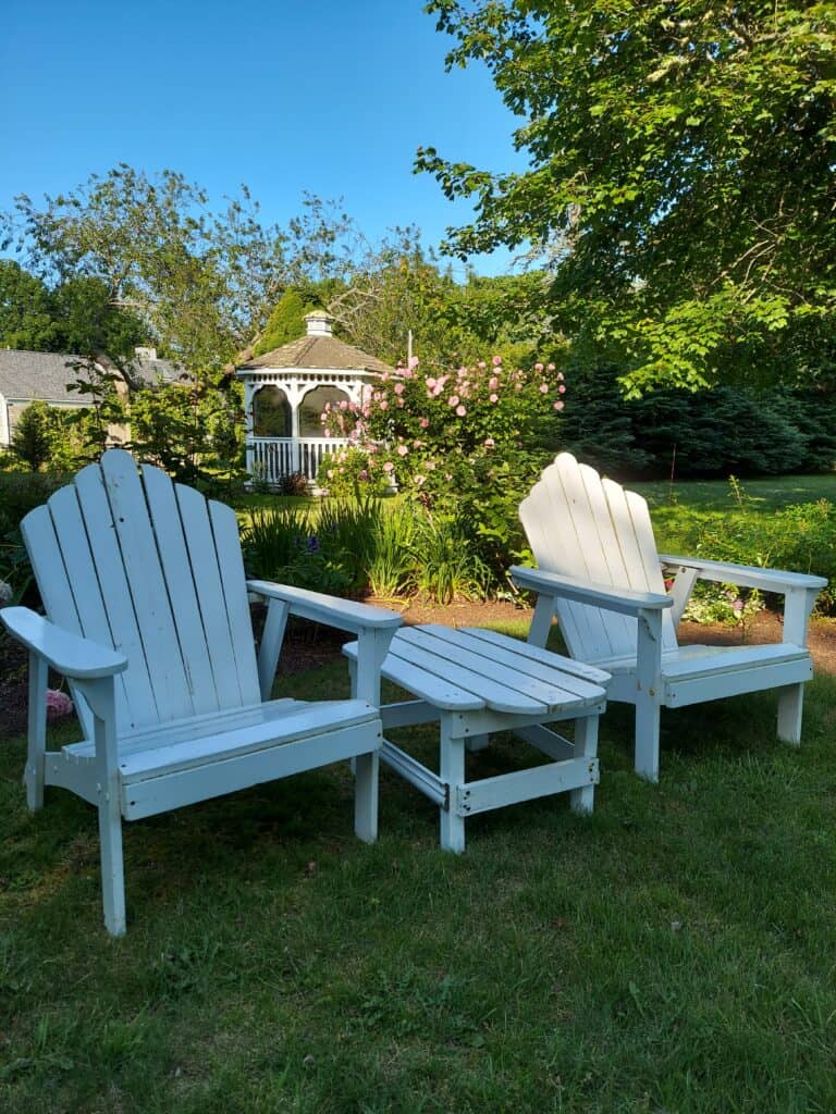 White adirondack chairs and a gazebo are seen in a lush green lawn in Chatham, Massachusetts on Cape Cod